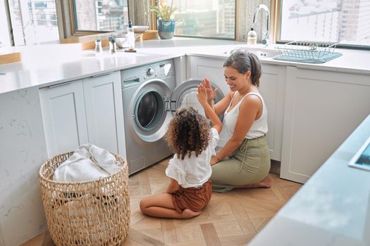Young hispanic mother and her daughter giving each other a high five after doing laundry at home. Adorable little girl helping her mother with household chores