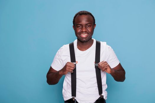 Happy young man pulling suspenders on blue background