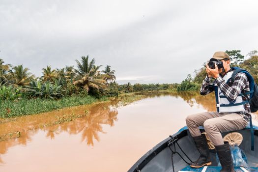Latino man sailing a boat down a muddy river and taking pictures