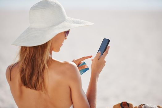 Woman using credit card on vacation. a young woman using her phone and credit card at the beach.