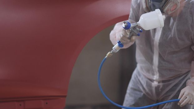 Red car in a paint chamber during repair work. Auto painting worker. Professional car painter is painting a body work. Male technician is air-painting car's door