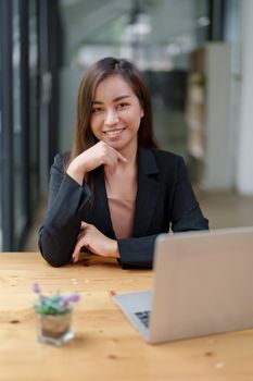 Portrait of a beautiful Asian businesswoman in a formal suit sits at her office desk with laptop computer in office