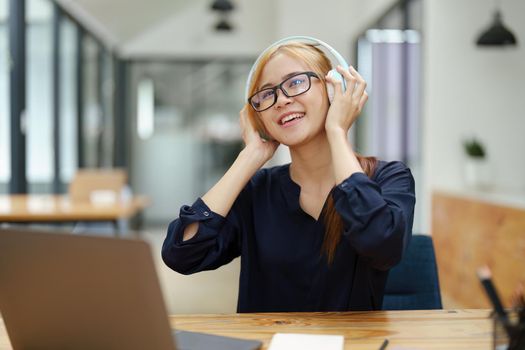 portrait of a young Asian woman with blonde hair wearing over-ear headphones listening to music to relax while taking a break from boring day activities