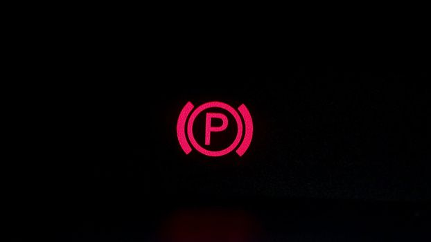 Parking brake control light in car dashboard. Close up of car's parking brake light coming on, on the dashboard