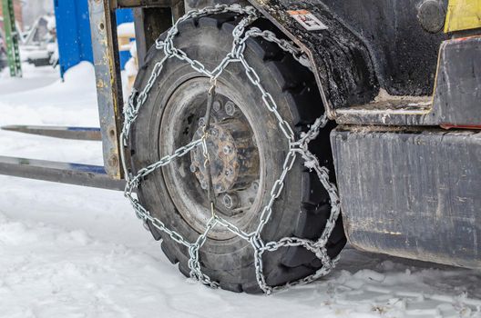 The loader is driving in the snow, the wheels are equipped with chains. Winter snowy day.