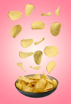Corrugated fried potato chips falling into a gray plate on a pink background