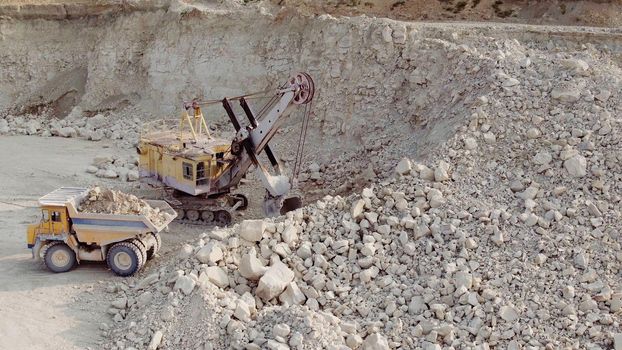 An excavator loads soil into a mining dump truck. Equipment for the extraction of iron ore in a quarry. The process of mining iron ore in a quarry. The smart process in an iron ore quarry