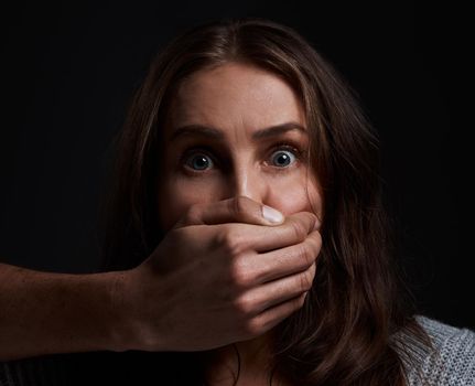 Ive been silenced all my life. a scared young womans mouth being covered by an unrecognisable mans hand against a black background.