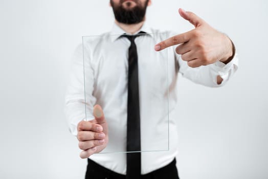 Male Corporate Holding And Pointing At Transparent Glass Presenting Important Sales Data. Businessman Wearing Necktie Displaying New Ideas And Strategies For The Branding.