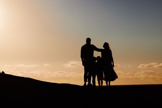 Silhouette couple with little kids standing outside at sunset. Family bonding and enjoying free time on a weekend outdoors and watching a sunset. Children with their mother and father on a weekend
