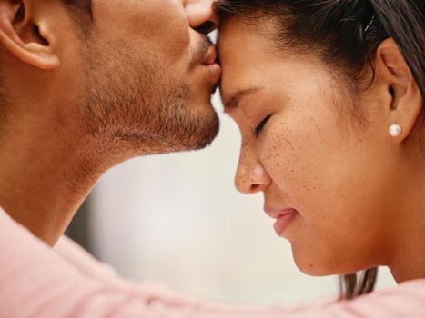 Closeup of mixed race man kissing his girlfriends forehead. Headshot of hispanic couple bonding and sharing an intimate moment at home. Beautiful woman with freckles feeling in love with boyfriend