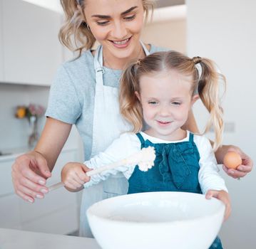 Mother and daughter baking at home. Happy mother and child bonding and cooking. Woman helping her daughter make batter. Young mother holding an egg, baking with her little girl.