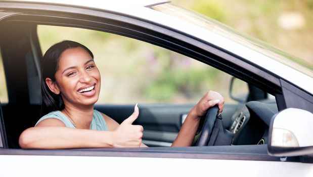 Cheerful mixed race woman showing thumbs up while driving her new car. Woman looking happy after buying her first car or after passing her drivers test. Car insurance
