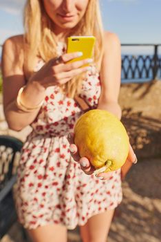 Look at the size of this citron. an unrecognisable woman standing alone and using her cellphone to photograph a citron in Italy.