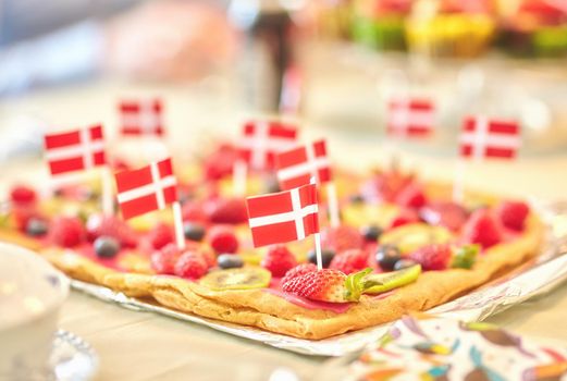 Danish fruit pastry for dessert to celebrate patriotism on Constitution Day in June. Annual holiday feast in Denmark with national flags in food. Fresh summer produce on a baked puff pastry