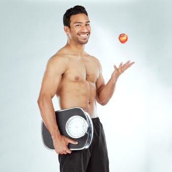 Keeping the scales in check. a young man holding a scale and an apple against a studio background.