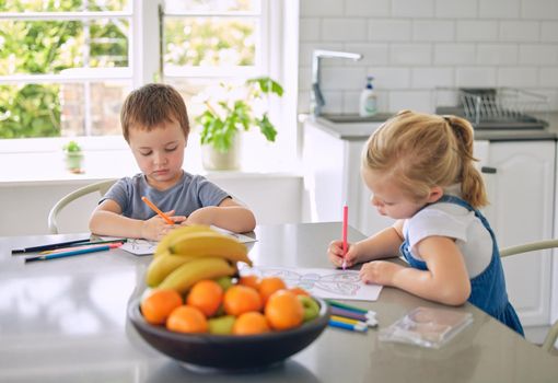 Caucasian siblings drawing pictures together. Brother and sister doing homework. Children colouring in sketches in their kitchen. Little girl drawing with her brother.Kids drawing art