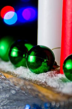 Red and white candle with a green New Year's ball on the background of lights