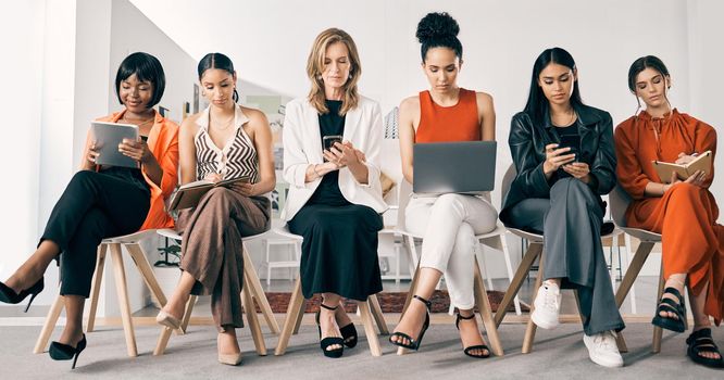 Lets get down to work. a group of businesswomen sitting in a row in an office at work.