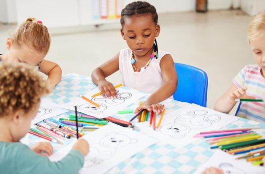 Diverse group of children sitting at a table and colouring at pre-school or kindergarten. Group of kids with colourful pencils and pictures