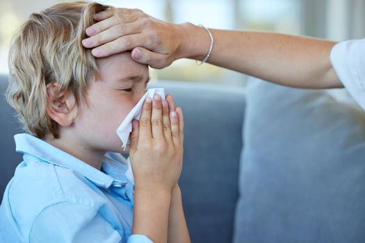 Sick boy blowing nose. Mother feeling sons head for a fever. Little boy with a cold blowing his nose into a tissue. Parent caring for an ill child. Worried mother checking sons temperature