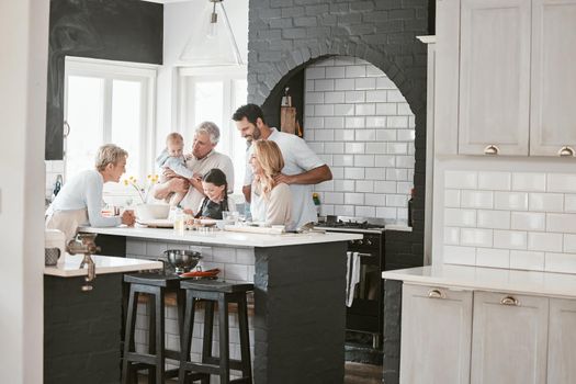 . Multi-generation caucasian family baking together in kitchen. Happy extended family baking a cake with ingredients on a table at home. Little girl baking with her parents and grandparents.