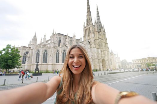 Woman in great mood takes selfie photo in front of Bordeaux Cathedral, France