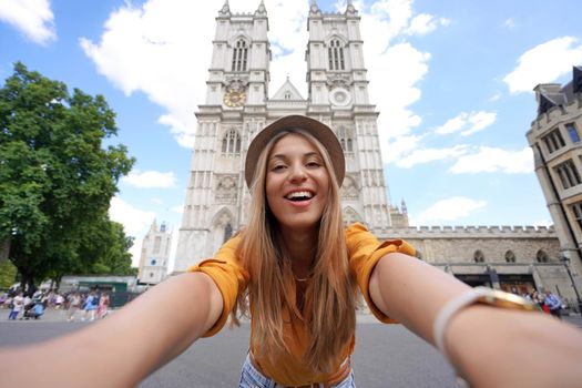 Young traveler girl taking selfie photo in London with Westminster Abbey gothic church. Young woman enjoying holidays in London, England.