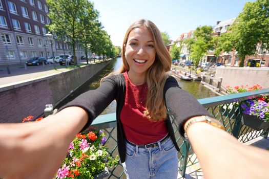 Pretty girl in Netherlands on sunny day. Smiling young woman takes selfie picture on canal in The Hague, Netherlands.