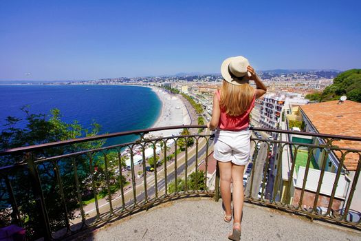 French Riviera. Back view of attractive young woman holding hat enjoying view of the cityscape of Nice, France.