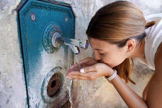 Close up of young woman hydrates herself from a fountain during a heat wave in the city