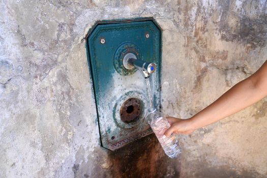 Woman hand fills a plastic bottle of water from a fountain in the wall. Thirsty and water crisis concept.