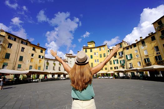 Holidays in Tuscany. Young tourist woman raising arms in the historic round square Piazza Anfiteatro in Lucca, Tuscany, Italy.