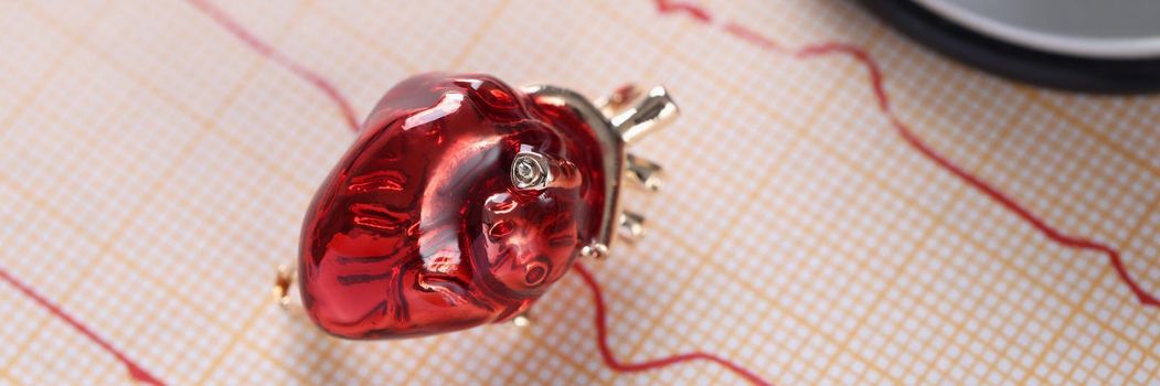 Red glass miniature heart toy lay over heart cardiogram result
