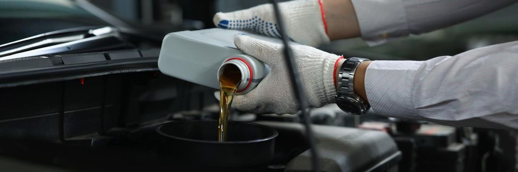Worker refueling and pouring new oil into engine motor of automobile