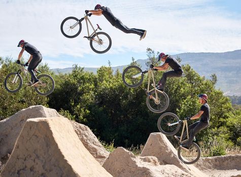Young man showing his cycling skills while out cycling on a bicycle outside. Adrenaline junkie practicing a dirt jump outdoors. Male wearing a helmet doing extreme sports with a bike. Phases of a jump