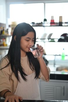 Asian girl drinking clean mineral water from glass. Healthy lifestyle concept.