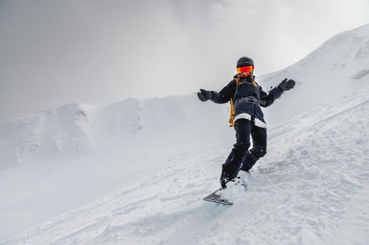 Young stylish girl or woman in motion snowboarding in the mountains