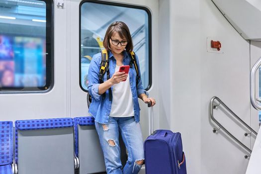 Woman passenger with suitcase backpack standing inside the car, commuter train