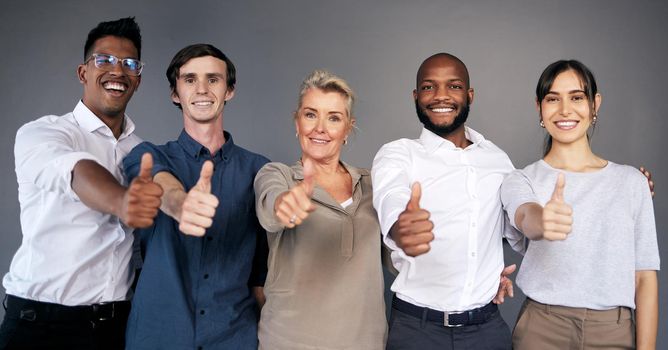 Teamwork begins by building trust. a group of workers showing a thumbs up in a office.