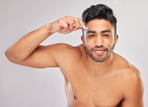 Getting the perfect shape. a young man plucking his eyebrows against a grey background.