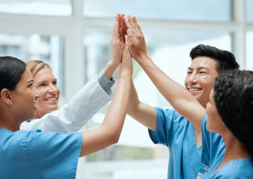 There is comfort in numbers. a group of medical practitioners joining hands to high five each other at work.
