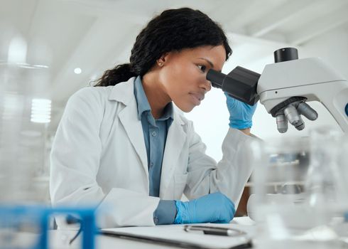 Working without any distractions. a young woman using a microscope in a scientific lab.