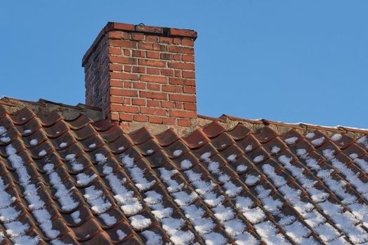 Red brick chimney designed on the roof of a snow covered residential house or building against a clear sky background. Air vent construction for the release of smoke and heat from fireplace in winter