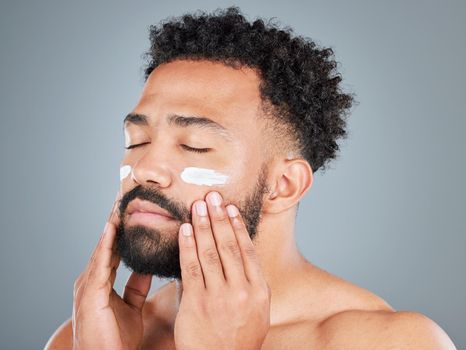 Loving the condition of his skin. Studio shot of a handsome young man applying lotion to his face against a grey background.