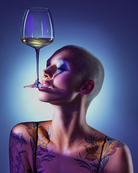 Im a goddess thats as fine as wine. Studio shot of an attractive young woman wearing edgy makeup and holding a glass of wine in her mouth against a blue background.