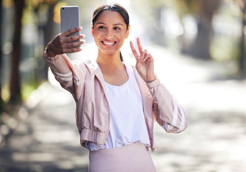 Wishing you all a healthy and safe day. a sporty young woman making a peace sign and taking selfies while exercising outdoors.