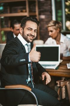 Smiling businessman shows Thumbs Up gesture sitting at Meeting