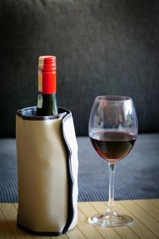 Red wine bottle with thermo cooler and wineglass on wooden background