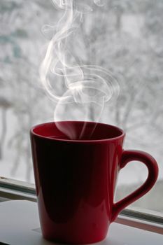 Hot tea in the red mug by the window on a snowy day